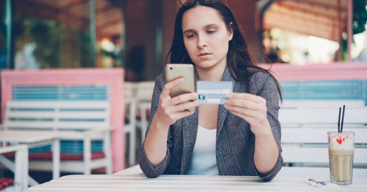 A person managing money on a phone with a bank card at a cafe