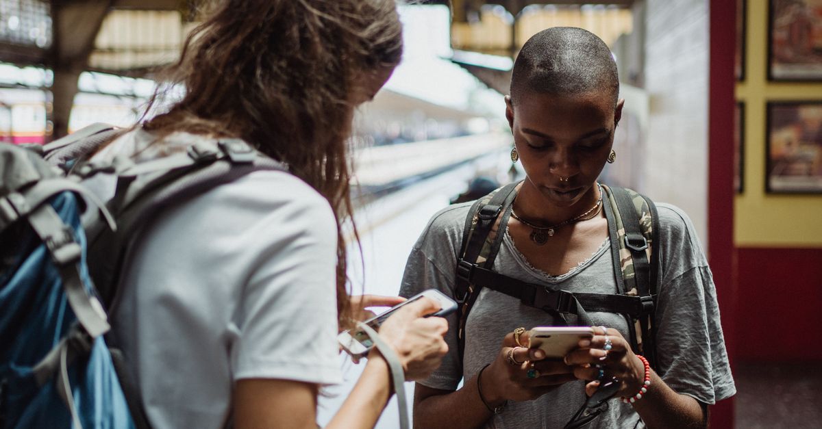 Two backpackers checking their phones at a railway station abroad