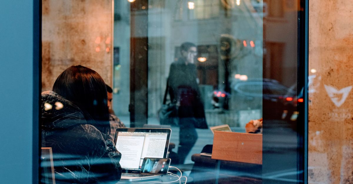 A digital nomad working on a laptop in a cafe, seen through the window